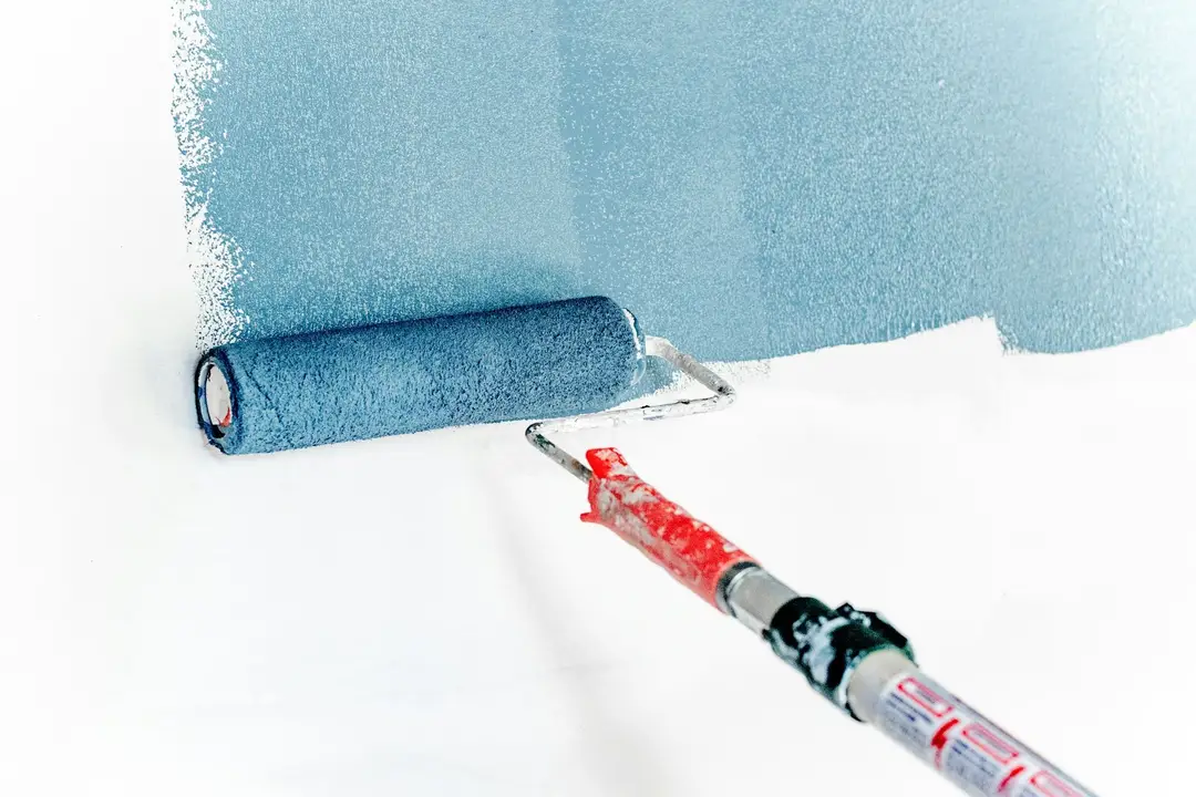 Roller applying blue paint over a white wall