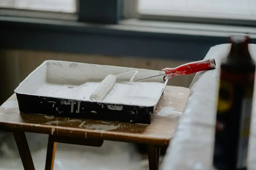 Paint roller resting in a tray of white paint